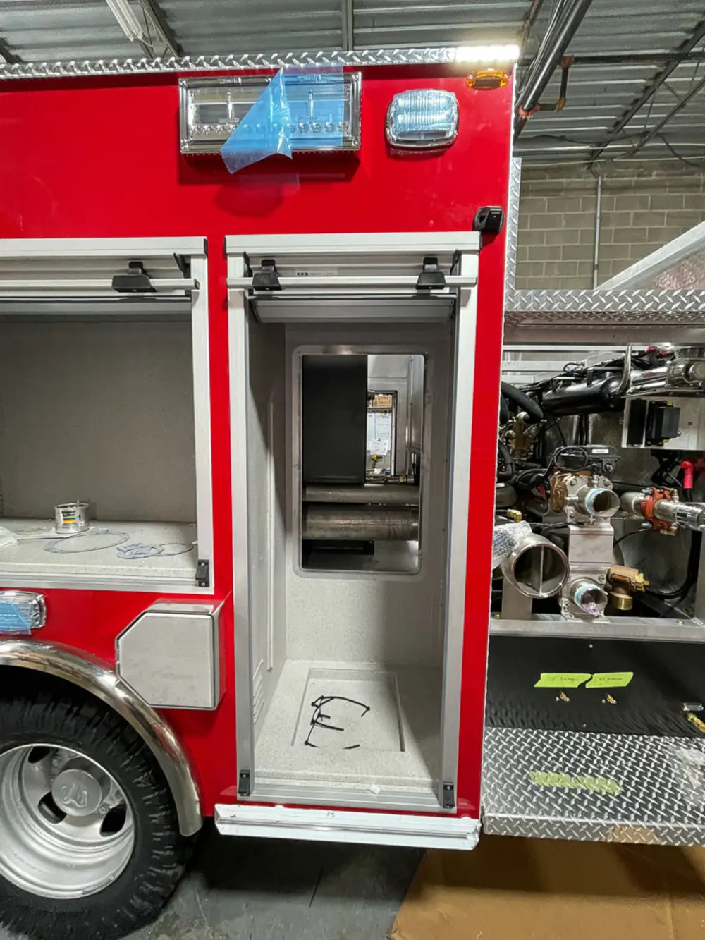 Exterior view of small fire truck showing cab, body compartments, and wheel/tire area.